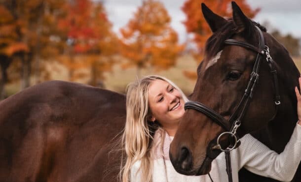 A woman standing with a bay horse in an autumn field.