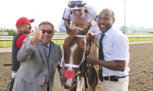 Two smiling men posing with a jockey on a chestnut racehorse.