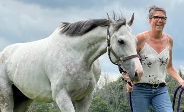 A woman leading a grey horse.