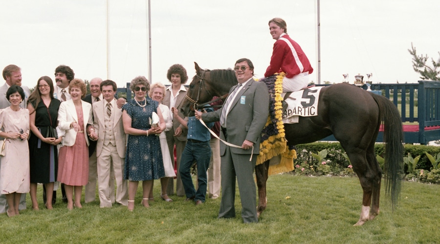An old photo of a horse and jockey with connections in the winners circle.