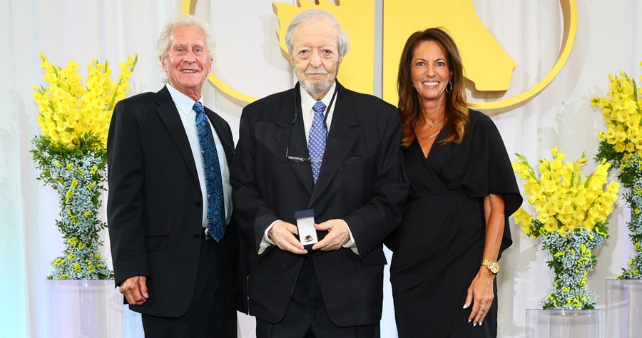A grey-haird man receiving an award, flanked by a man and woman.