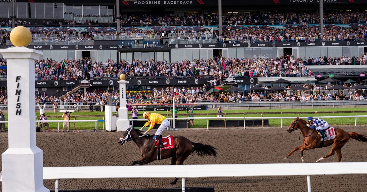 Horses crossing the finish line at Woodbine with a large crowd in the stands.