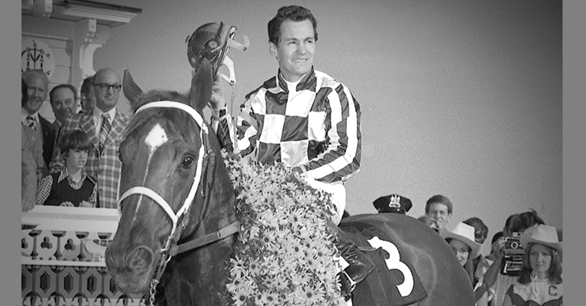 A black-and-white photo of a jockey on a horse in the winners circle.