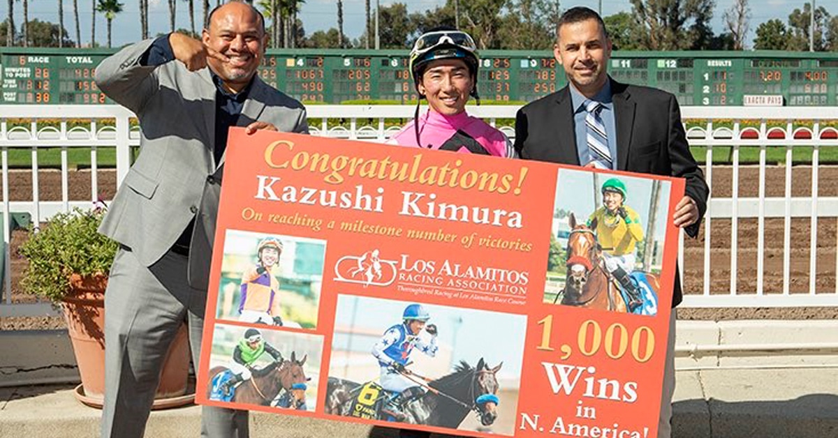 A jockey with two men holding a large poster.