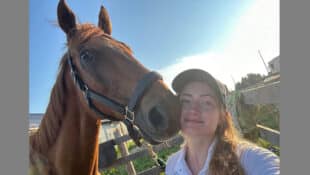 A young woman taking a selfie with a chestnut Thoroughbred.