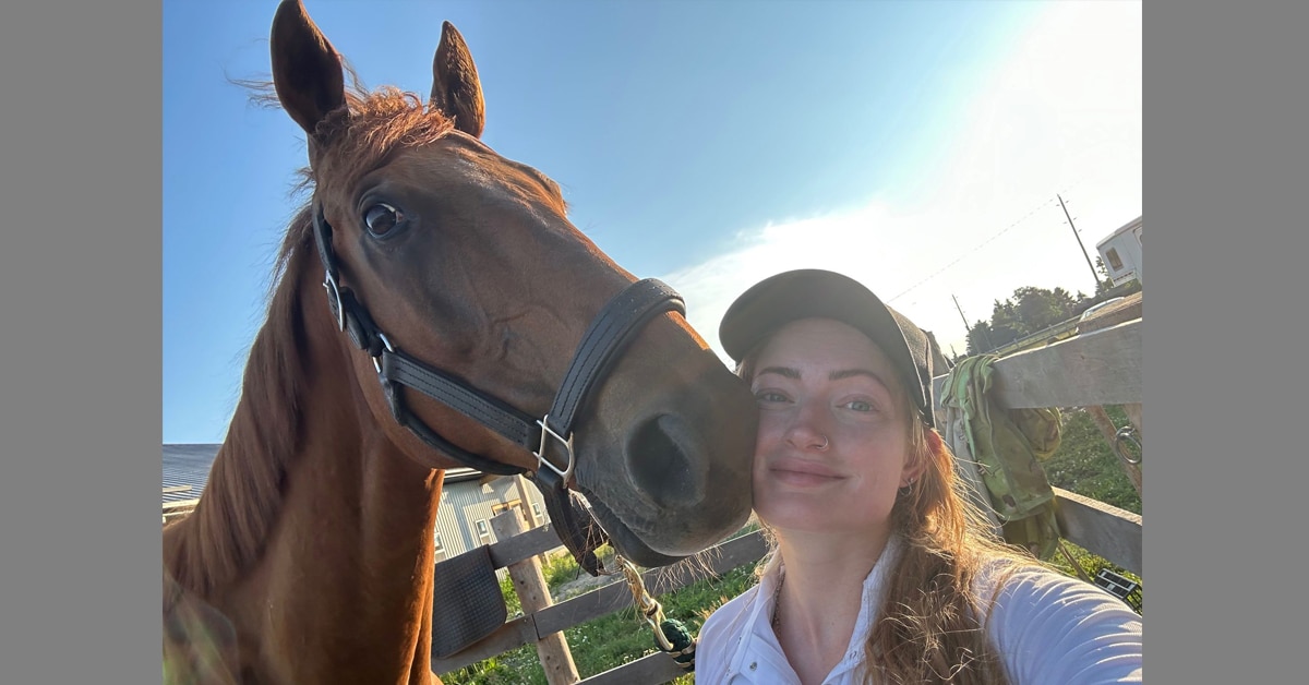 A young woman taking a selfie with a chestnut Thoroughbred.