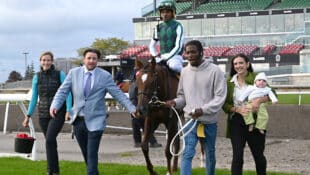 A man accompanied by two other people leading a bay mare and jockey to the winner's circle at Woodbine.