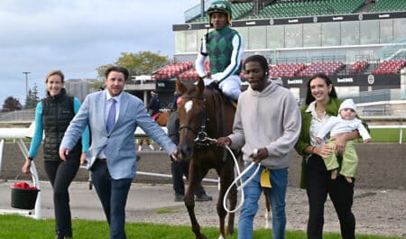 A man accompanied by two other people leading a bay mare and jockey to the winner's circle at Woodbine.