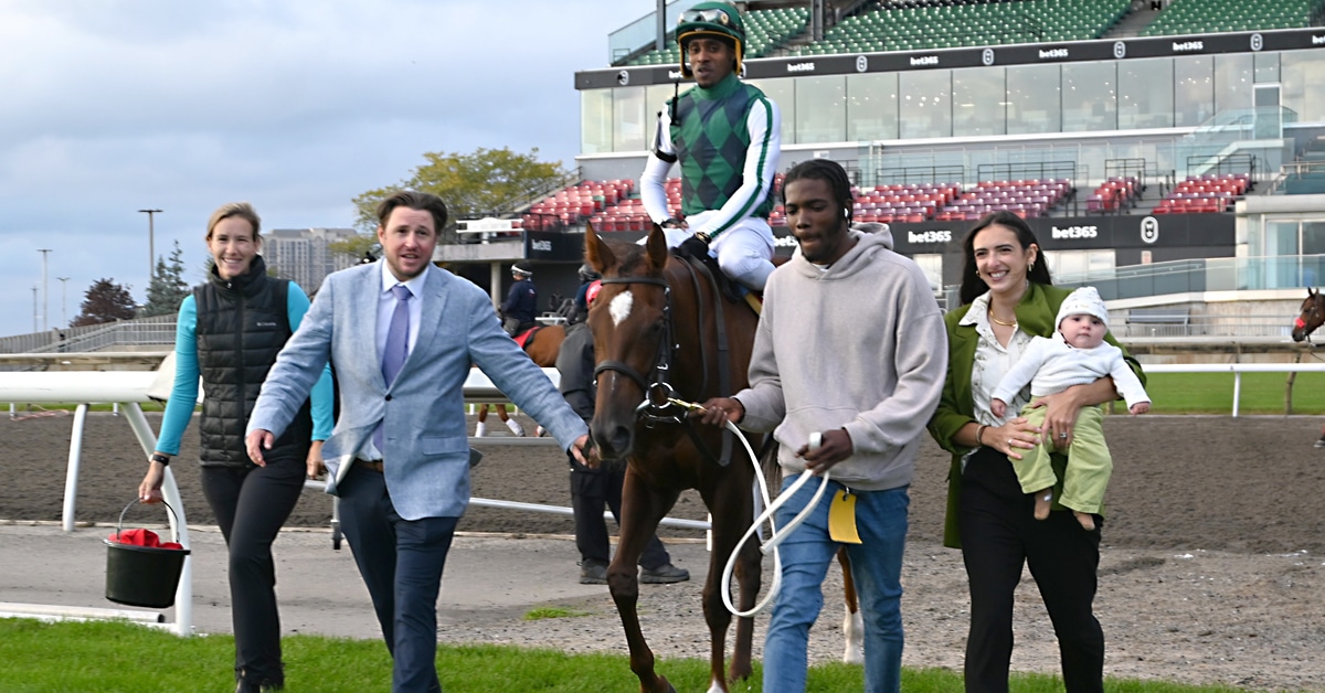 A man accompanied by two other people leading a bay mare and jockey to the winner's circle at Woodbine.