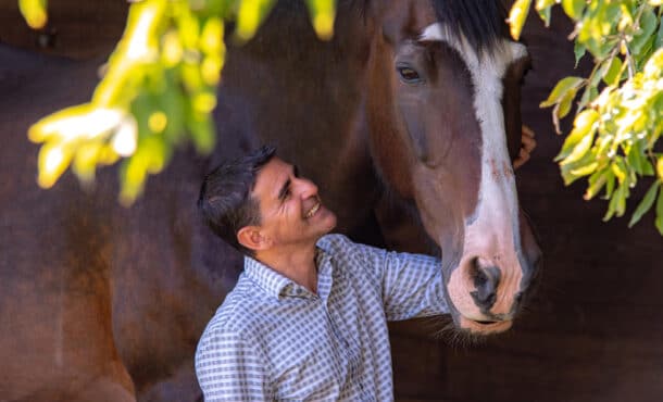 A smiling man patting a bay horse.