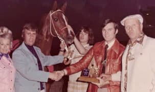 A very old colour photo of a group of people in the winners circle.