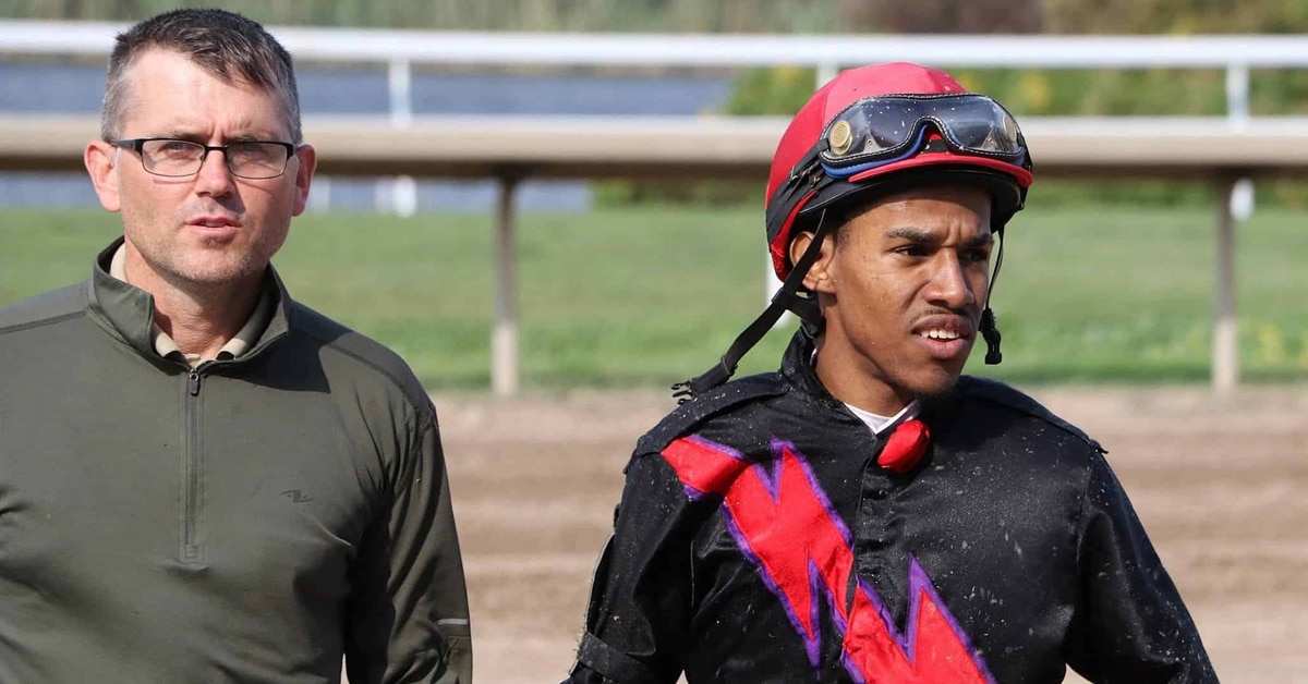 A man and a jockey standing on the side of a racetrack.