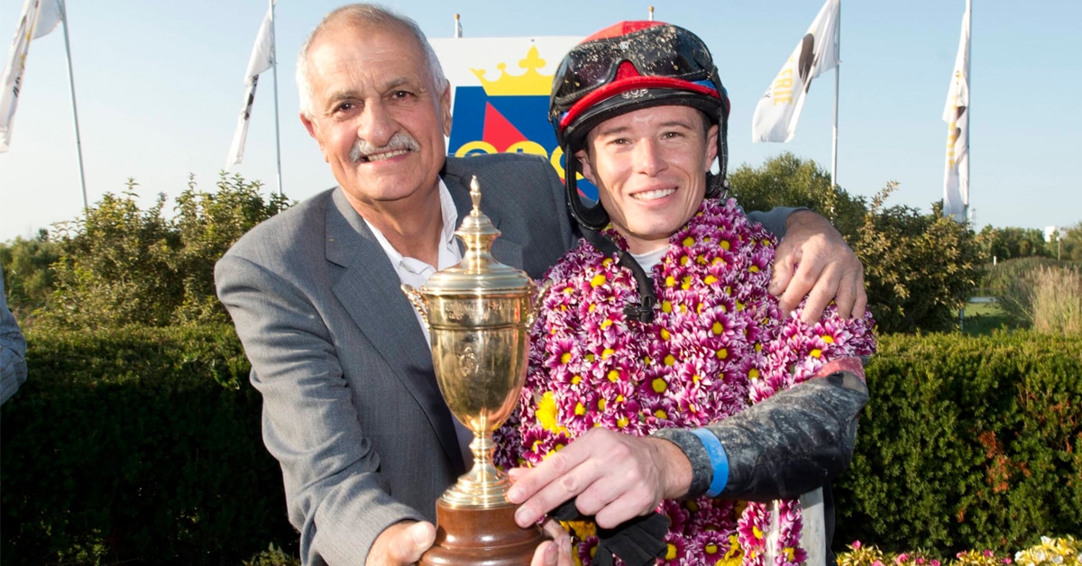 A grey-haired man and a jockey holding a trophy.