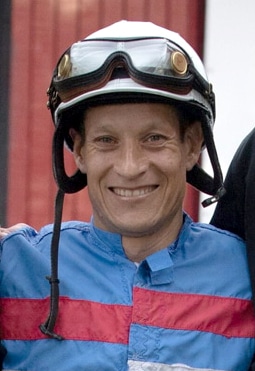 A smiling jockey wearing blue and red silks.