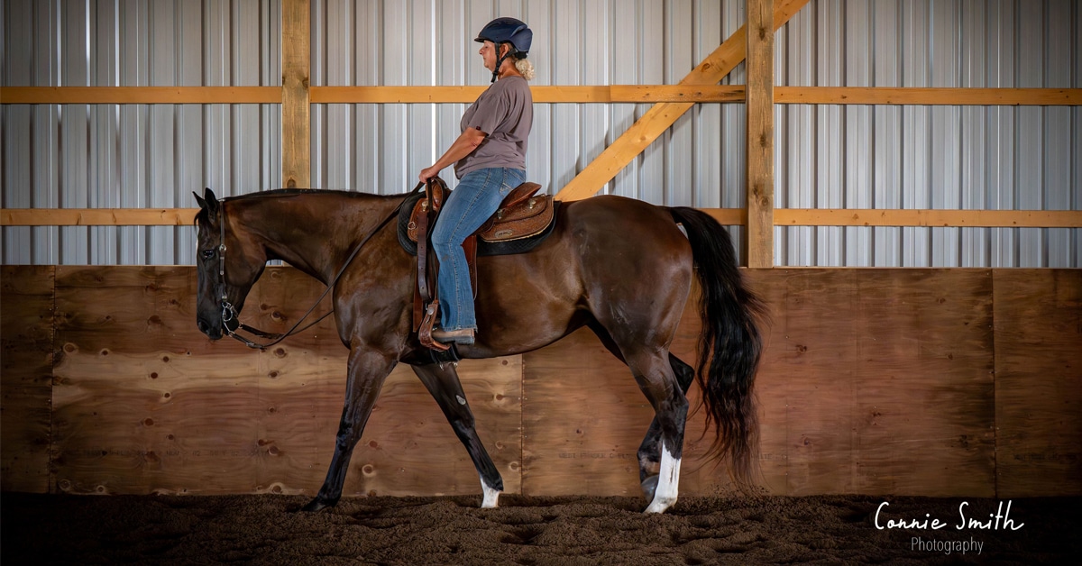 A woman riding a dark chestnut in a western saddle, in an arena.