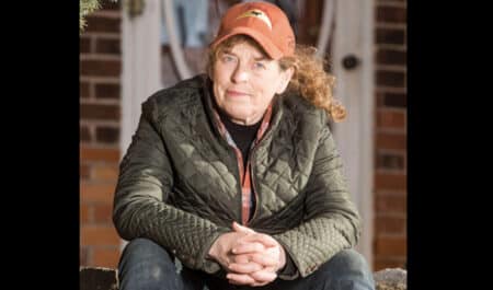 A woman sitting with clasped hands, wearing an orange hat.