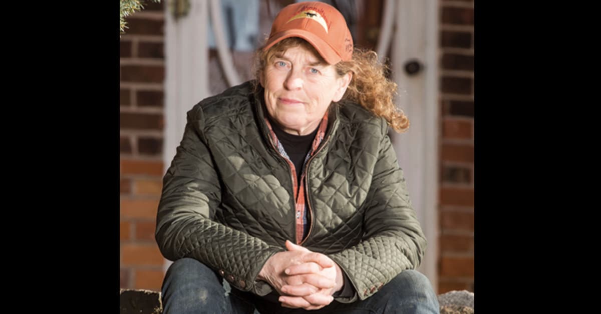 A woman sitting with clasped hands, wearing an orange hat.