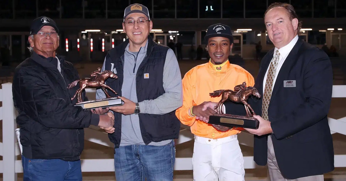 Two men receiving trophies from two other men at a racetrack.