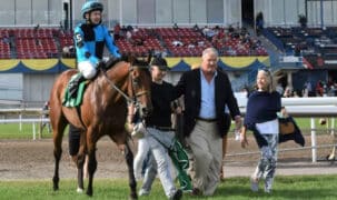 Two men and a woman leading a horse and jockey into the winners circle at Woodbine.
