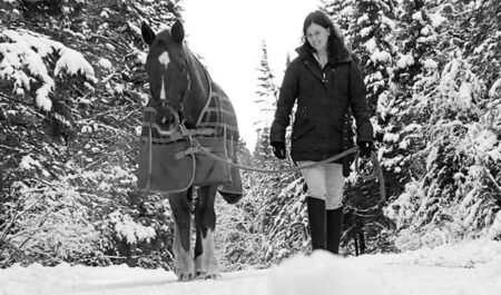 A black-and-white photo of a woman leading a horse through the snow.