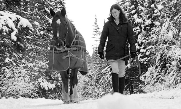 A black-and-white photo of a woman leading a horse through the snow.