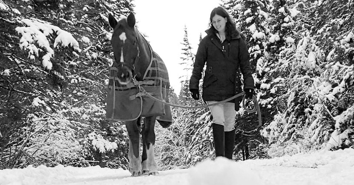 A black-and-white photo of a woman leading a horse through the snow.