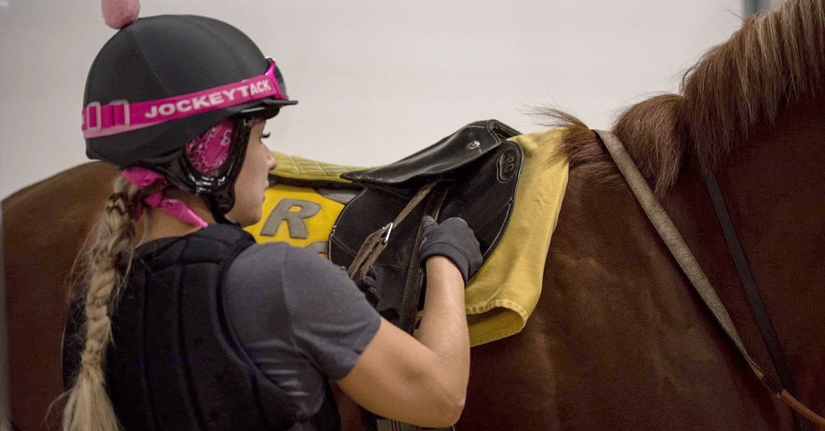 A woman saddling a racehorse.