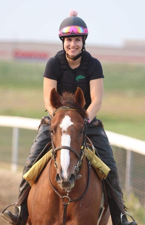 A smiling woman exercising a chestnut racehorse.