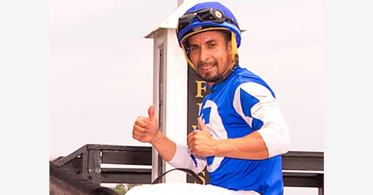 A jockey wearing blue silks, giving the thumbs-up.