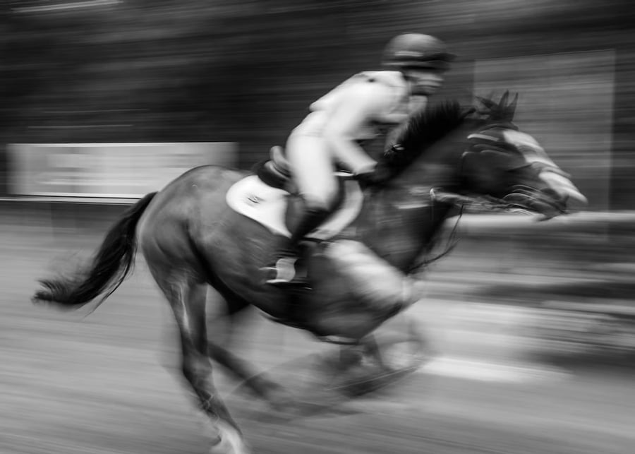 Blurred black-and-white image of a racehorse and jockey.