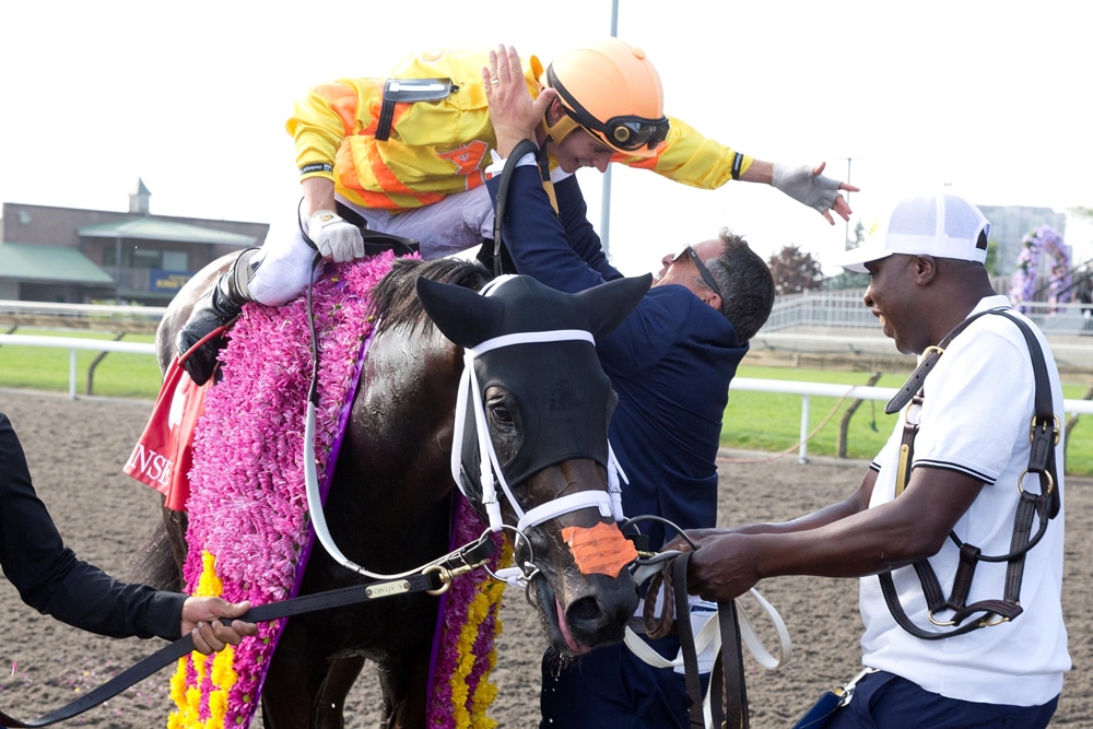 A trainer hugging a jockey on a racehorse.