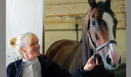 A woman holding a racehorse in a barn.