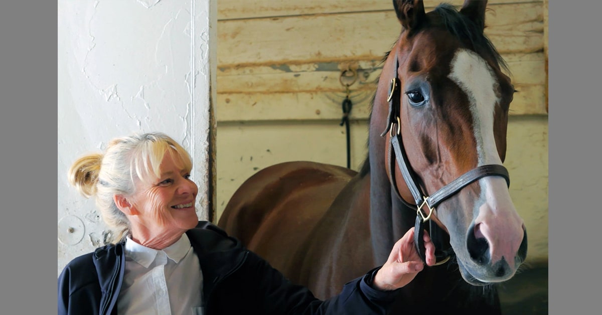 A woman holding a racehorse in a barn.