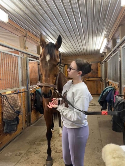 A young woman in a barn aisle with a bay horse.