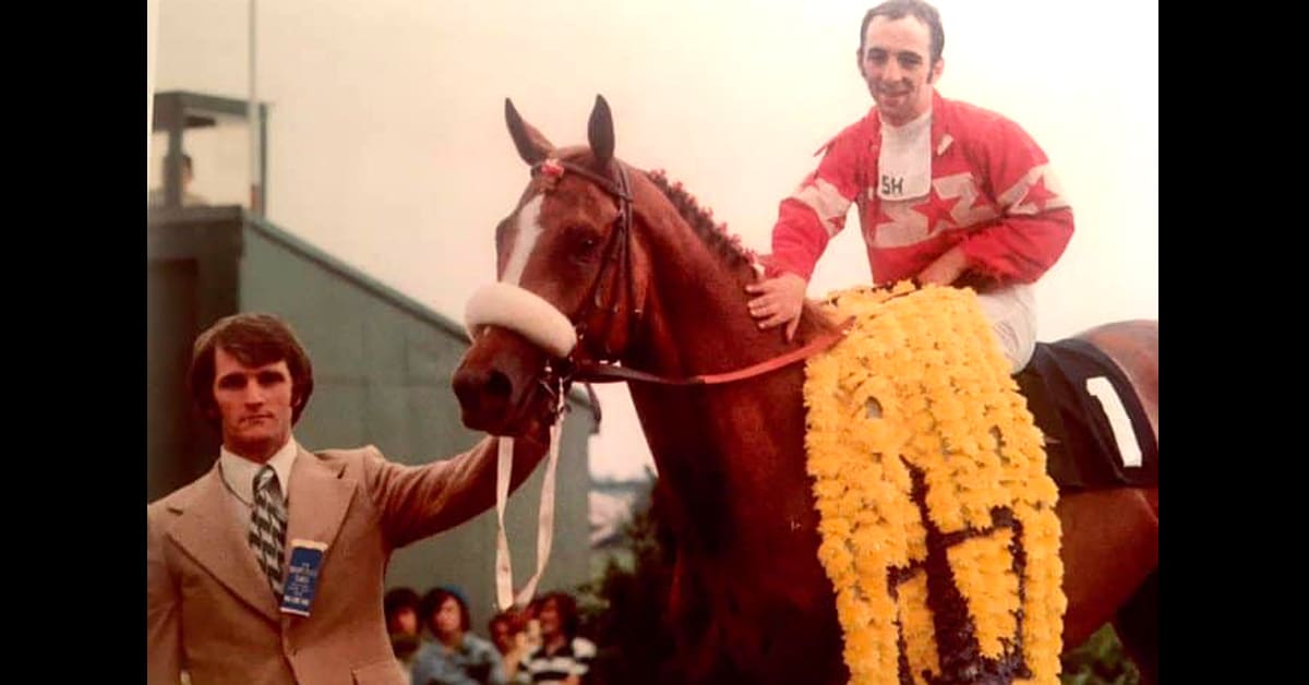 An old photo of a man leading a horse and jockey to the winners' circle.