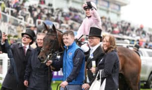 A group of people with a horse and jockey in the winners circle.