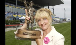 A woman holding up a trophy at the racetrack.