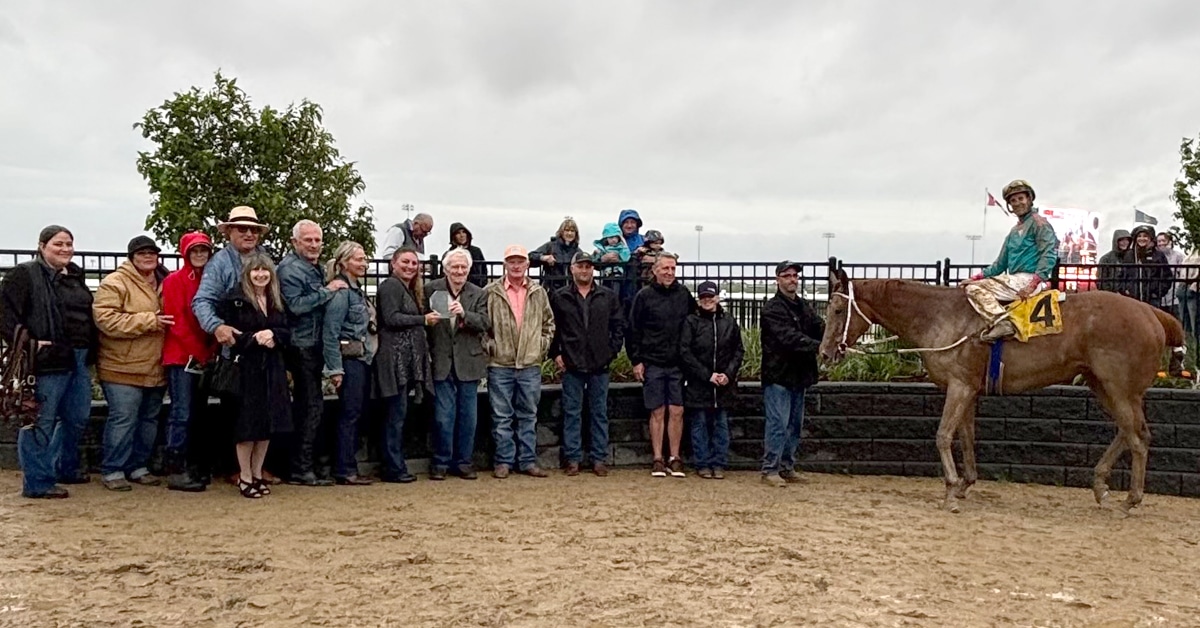 A winners circle photo with a group of people and a muddy horse.