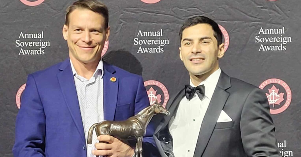 A man presenting another man with a Sovereign Award trophy.