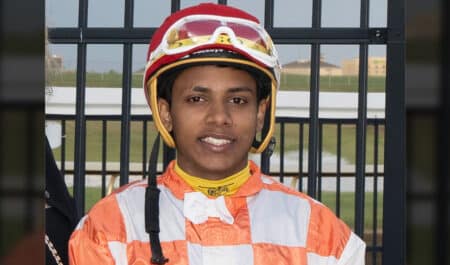 A young smiling jockey in orange and white silks.