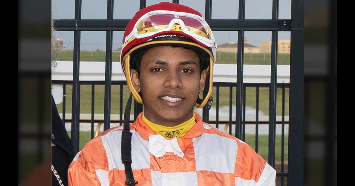 A young smiling jockey in orange and white silks.
