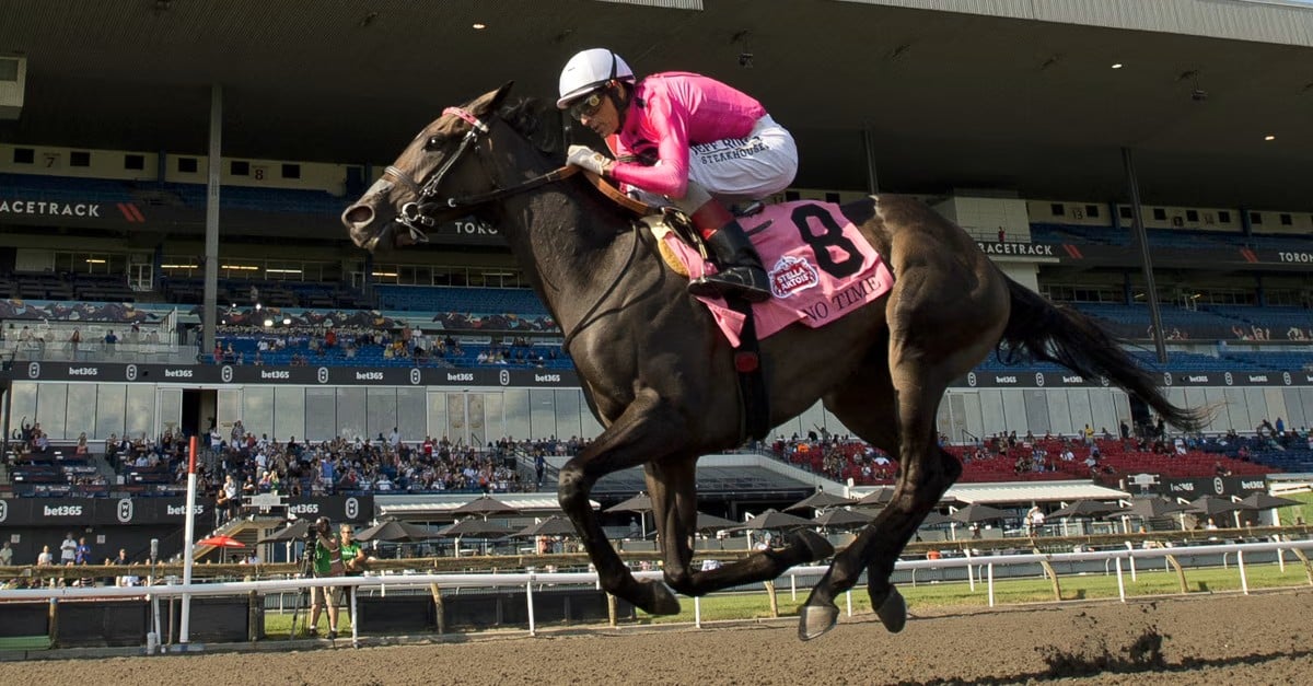 A jockey with pink silks riding a horse to the finish line at Woodbine.