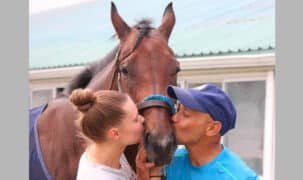 A man and woman kissing a bay racehorse.