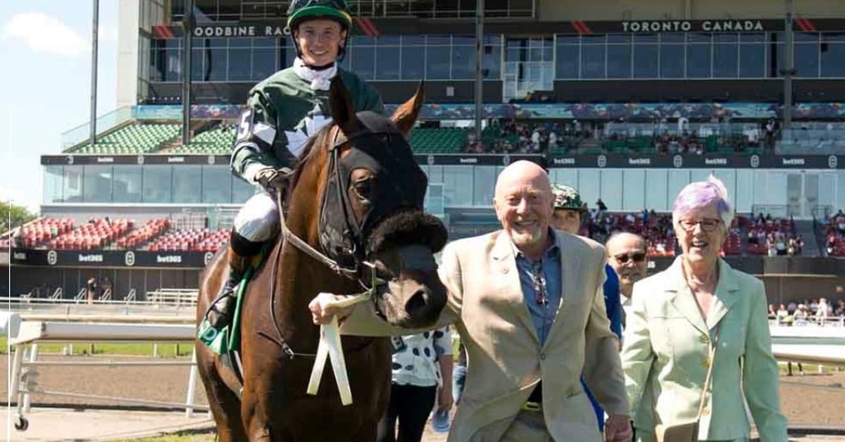 A smiling man and woman leading a horse and jockey into the winners circle at Woodbine.