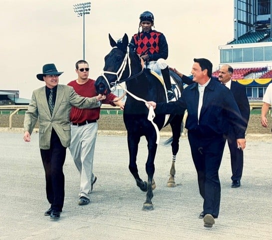 A horse being led into the winners circle by a group of men.