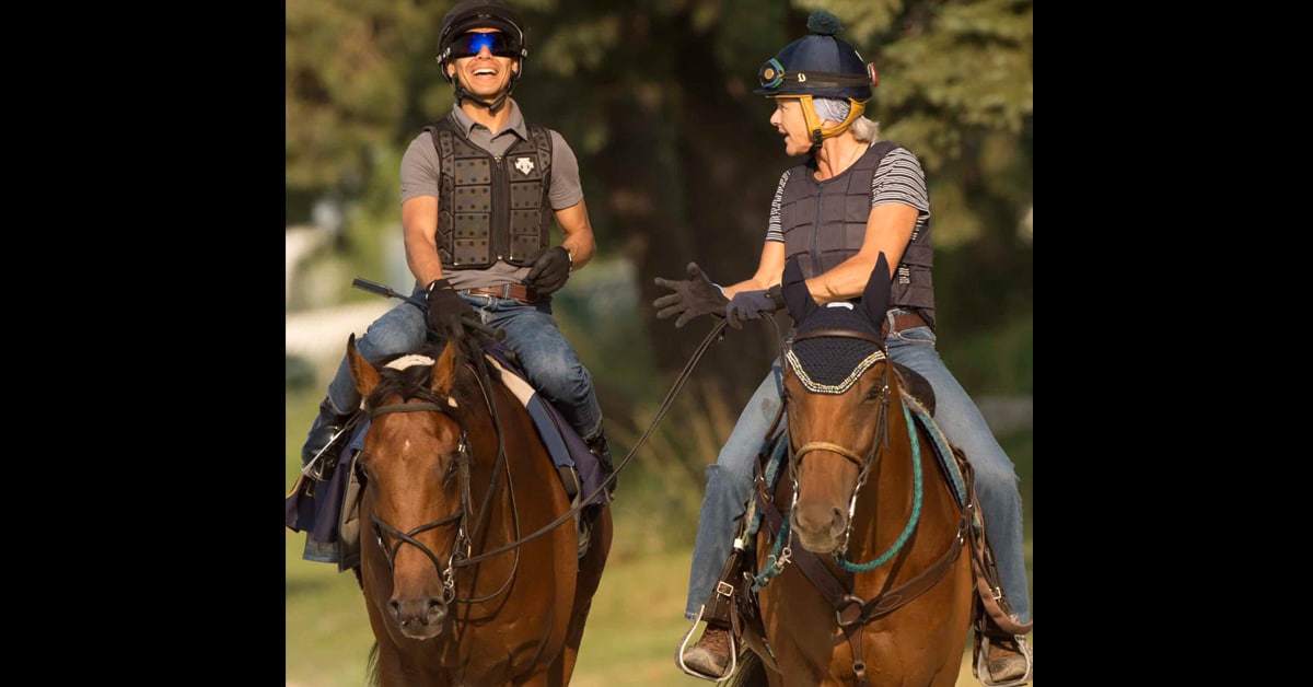 Two riders on racehorses, talking and laughing.