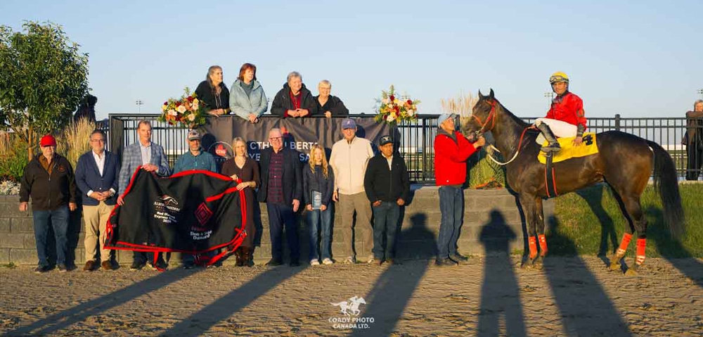 A large group of people with a bay horse in a winners circle photo.