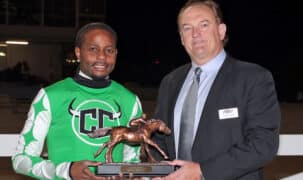 A man handing a trophy to a jockey.