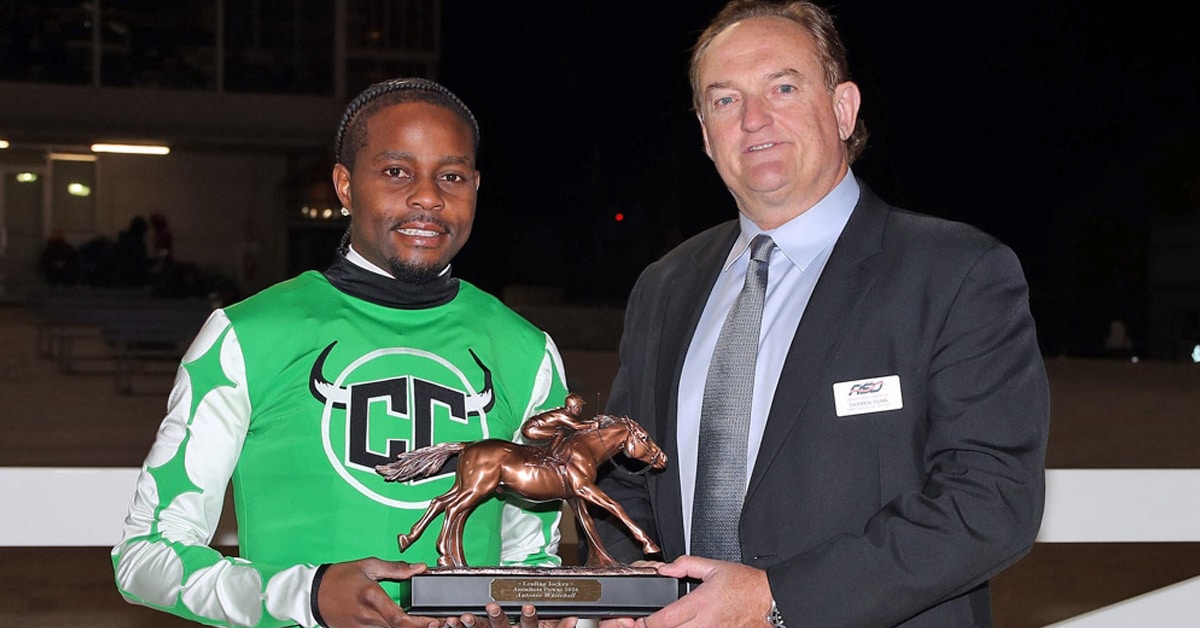 A man handing a trophy to a jockey.