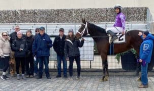 A group of people standing with a horse and jockey in the winners circle.